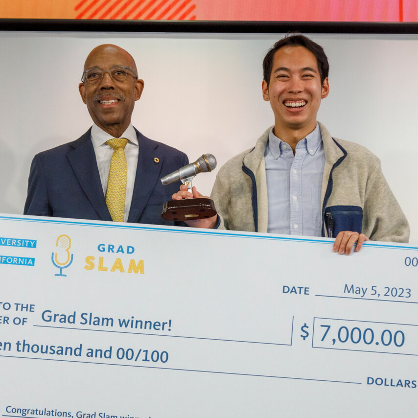 Brandon Tsai holding a giant check for his Grad Slam winnings, standing with University of California President Michael V. Drake.