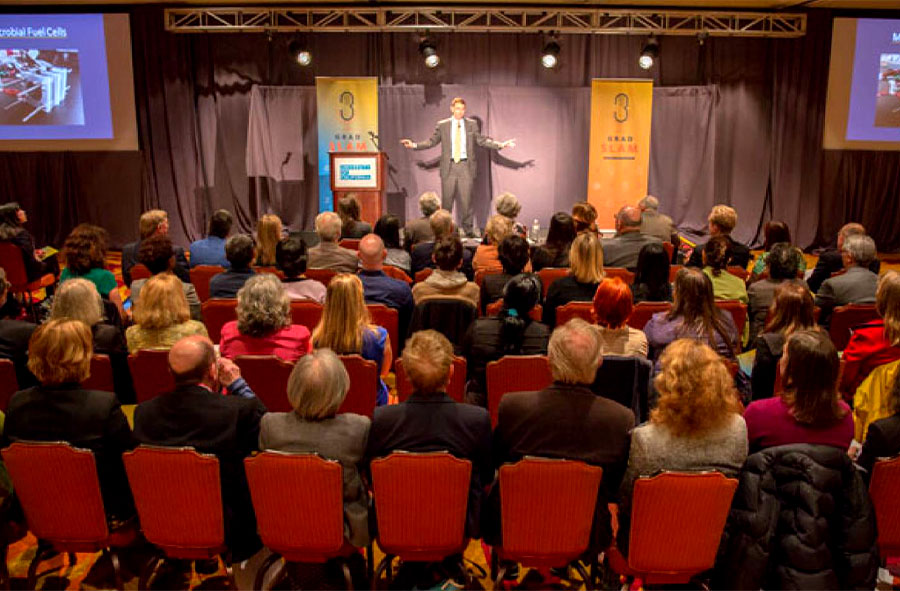 Seen from a vantage point behind the audience, a full view of the stage where Ryan Dowdy presents at Grad Slam 2015