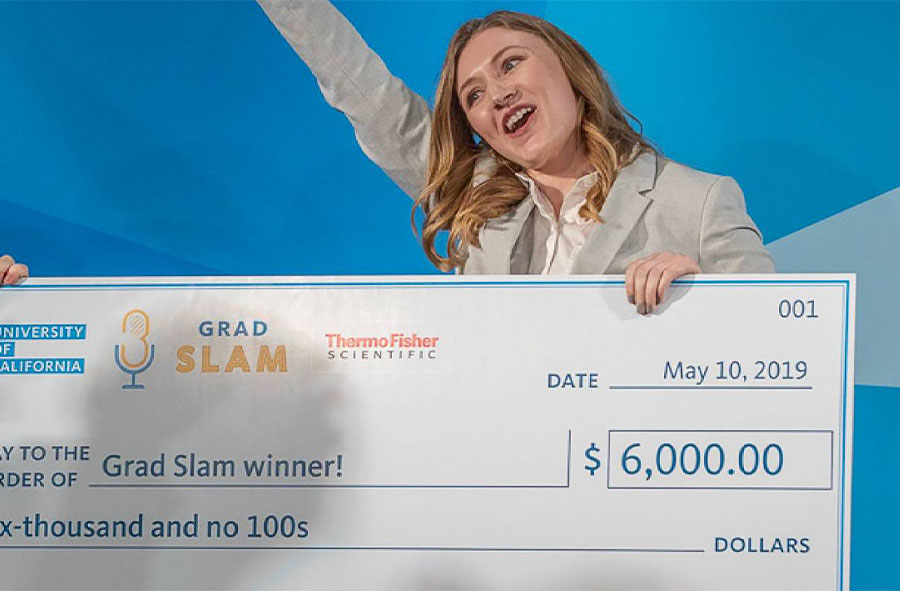 An exultant Katie Murphy raises one arm while holding her first place check after winning Grad Slam 2019
