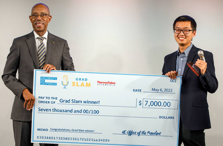 University of California President Michael V. Drake holds one corner of the winner's check while Grad Slam 2022 winner Justin Lee holds the other in one hand and the Slammy trophy in the other